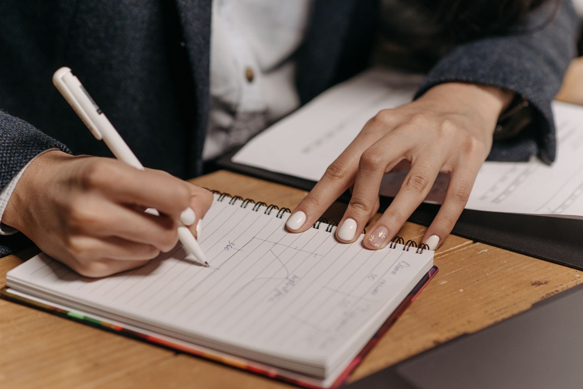 Close-up of a person writing notes in a notebook at a desk — the focused work that good systems enable
